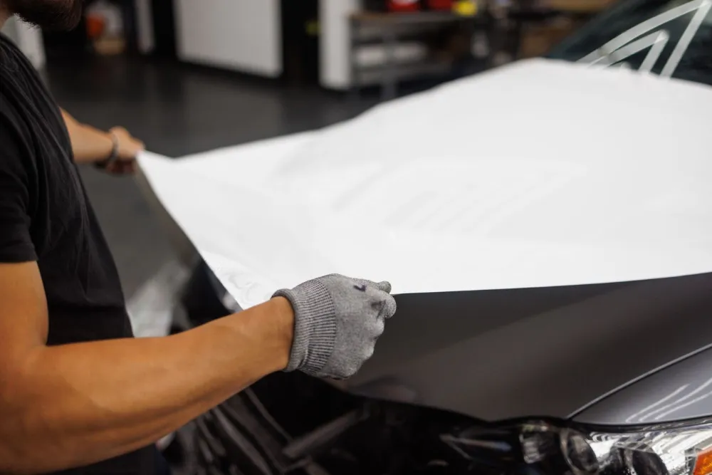Gloved hands smoothing white vinyl onto a car bonnet